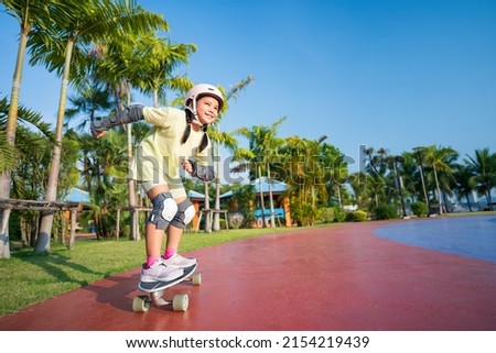 asian child or kid girl smile playing surf skate or skateboard in skatepark and extreme sports exercise to wearing helmet elbow pads wrist and knee support for body safety protect at bang phra park Royalty-Free Stock Photo #2154219439