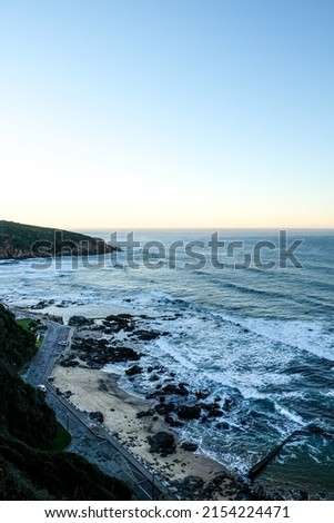 Portrait shot of the majestic Herolds bay from the perspective of the mountain next to the cross in the early morning hours on a cold, winter day. Sun rising in the foreground and waves crashing. 