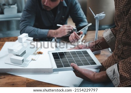 Energy engineer professionals discussion about calculating to use pure energy nature and Installing solar panels on roof house to generate electricity working with model, and Solar panel sample Royalty-Free Stock Photo #2154229797