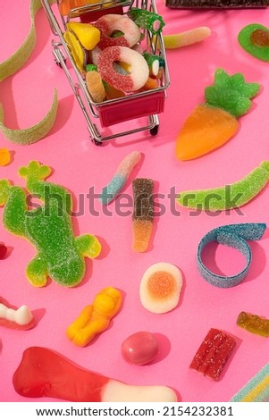marmalade sweets, a background of various kinds of jelly sweets in the form of bears, ribbons, fruits and other toys. Candies in a toy shopping cart. On a pink background.