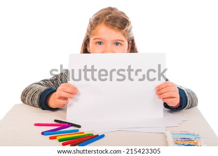 A little girl showing a piece of paper. Colored crayons and paint on the table.