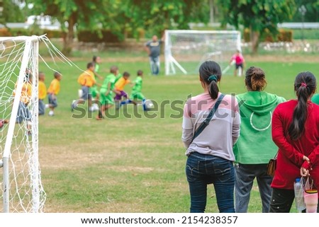 Back view of Moms watch and cheering their sons playing football in school tournament on sideline. Sport, outdoor active,  Spectator watching soccer game. Parents care and encourage their children. Royalty-Free Stock Photo #2154238357
