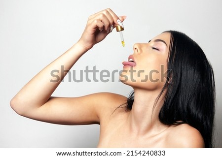 Herbal alternative medicine. Cannabis oil. Young woman taking CBD or dietary supplement drops in mouth from dropper. Cosmetic pipette with drops of CBD oil. Royalty-Free Stock Photo #2154240833
