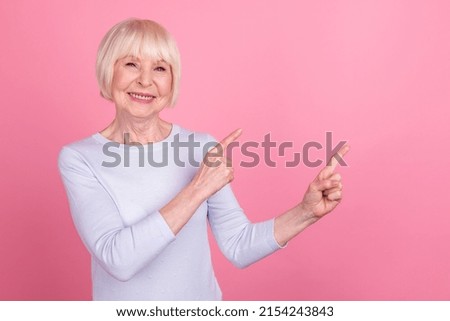Photo of lovely senior lady indicate fingers empty space promo choose ads banner isolated over pink color background
