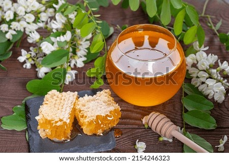 A cup with natural honey, honey in combs against the background of acacia flowers on a wooden table. The concept of wild bees honey and healthy sweets.