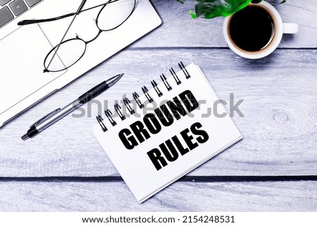 Laptop keyboard on wooden office table with coffee cup, computer mouse and notepad with GROUND RULES text. Business and finance concept. Workplace, flat lay with copy space.