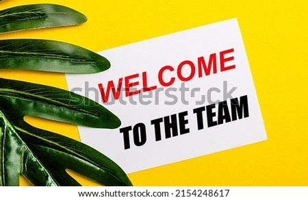 White sheet of paper with the inscription WELCOME TO THE TEAM on a bright yellow background near the green leaf of the plant. Eco natural banner concept