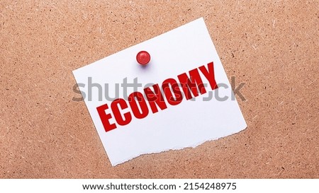 White paper with the text ECONOMY is attached to the wooden background with a red button.