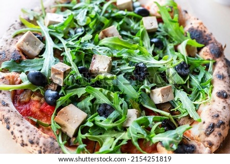 top view of vegan pizza with arugula or rucola tofu olives and tomatoes close-up wooden board vegetarian food healthy eating selective focus