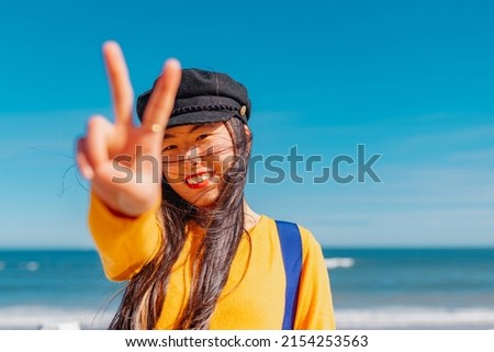 Asian girl making the peace or victory sign on the beach on a sunny day.