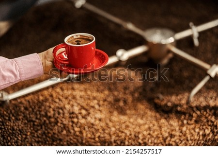 Cropped picture of hand with coffee cup next to a roasting machine.