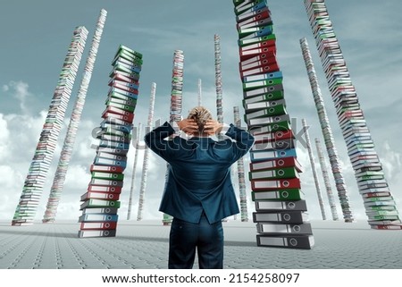 An unhappy office worker, a businessman, looks at the towers from many folders with documents. Concept of hard work, busy clerk, recycling, bureaucracy. mixed media. Royalty-Free Stock Photo #2154258097