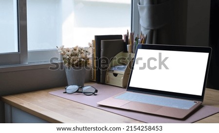 Contemporary workplace with computer laptop, glasses, coffee cup and supplies. Empty screen for graphics display montage.
