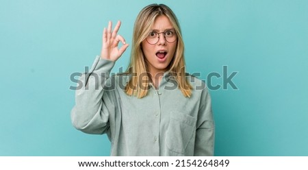 young pretty blonde woman feeling successful and satisfied, smiling with mouth wide open, making okay sign with hand