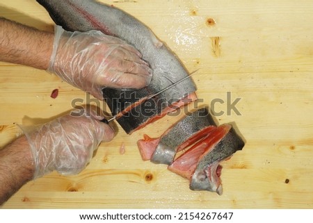 On the table, on a cutting board, is gutted fish from the salmon trout family, which the chef is cutting into steaks.                                