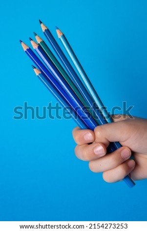 Child's hand holding blue colored pencils of different shades