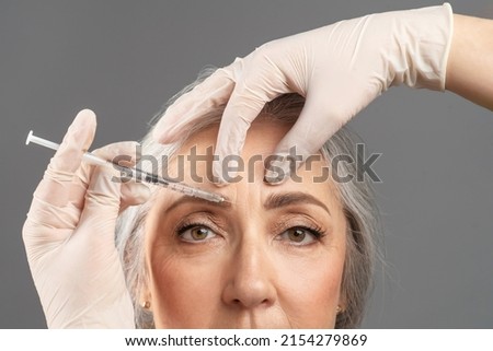 Mature skin rejuvenation. Closeup portrait of senior woman receiving cosmetic treatment with beauty injection on grey studio background. Beautician making anti-aging shot to older lady Royalty-Free Stock Photo #2154279869