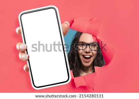 Wow, Great Offer. Amazed young lady holding big smartphone with isolated white screen in hand, showing close to camera through torn paper hole. Gadget with empty free copy space for mock up, template