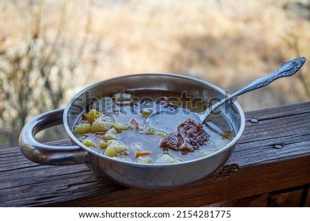 Stewed potatoes with meat in a metal camping cup. Dishes of the national cuisine of the peoples of the East. Tourist food. Horizontal photo of outdoor food.