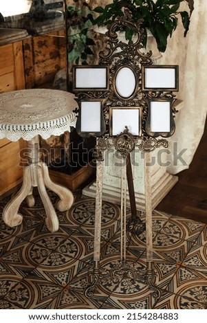 Wedding venue decorations, vintage baroque frames for guest notes. There is also a decorative table on the floor, against the background of wooden furniture and a stone column.
