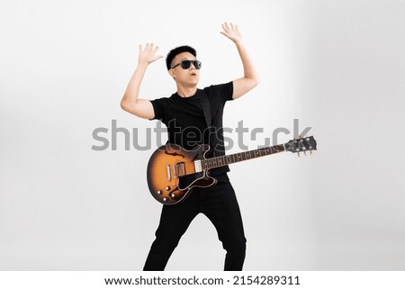 Young asian guy guitarist standing over isolated white background with a sunburst brown semi hollow body both hands up