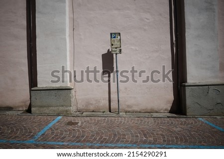 Old sign of paid parking by time and pointer to parking ticket in Italy. Parking space with blue markings on paved street and pointer to parking machine against pink wall in old town in Borgo Taro Royalty-Free Stock Photo #2154290291