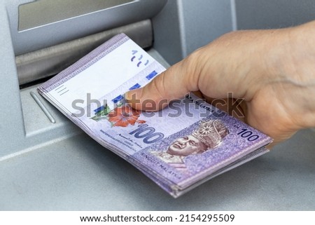 A woman chooses Malaysian ringgit from an ATM, The highest denomination, A lot of money, Economic and financial concept, Rising cost of living Royalty-Free Stock Photo #2154295509