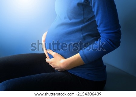 Close up of beautiful asian pregnant woman placing hands rubbing firmly on pregnant baby stomach, joyfully and happiness in mother hood sitting on the white bed sheets relaxing and resting in bedroom
