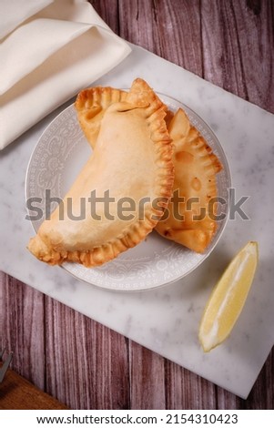 Empanadas traditional argentinian fried food stuffed with meat accompanied with lemon with a background of marble, wood and fabrics.