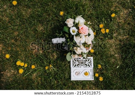 Golden rings on a white wooden box and a bouquet of flowers lie on the green grass. Wedding photography, top view.