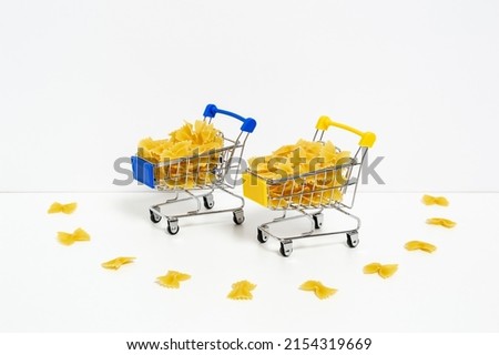 Uncooked farfalle pasta in blue and yellow shopping carts in colors of Ukrainian flag isolated on white background. Food supply crisis, price increase for wheat products, groceries shopping concept