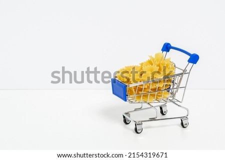 Farfalle pasta in blue shopping cart isolated on white background with copyspace for text. Food and groceries shopping, price increase, food crisis concept