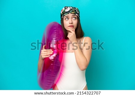 Young Ukrainian woman holding air mattress isolated on blue background having doubts and thinking