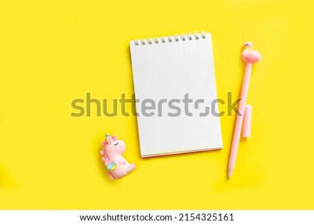 Unicorn. Blank white notepad on a spiral with a pink pen. Top view with copy space, flat lay on yellow background.