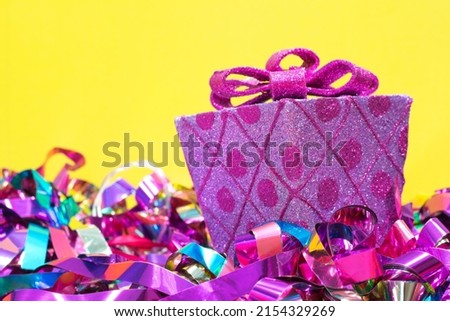 Wrapped decorative pink gift and bow with colored ribbons underneath on a yellow background with copy space.