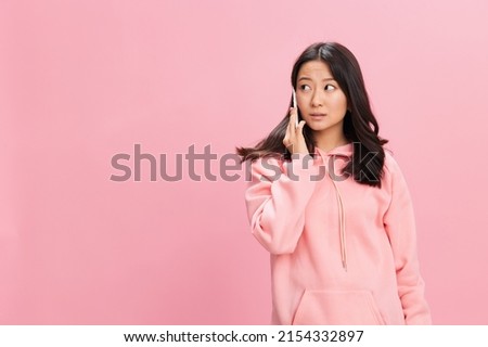 Confused unhappy cute Asian student young lady in pink hoodie sweatshirt get sad news from call posing isolated on over pink studio background. Good offer. Gadget addiction Social Media concept