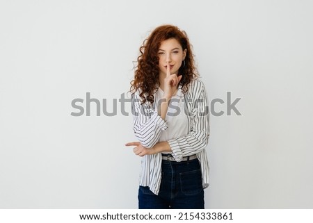 Photo of serious young redhead lady standing isolated over white wall background showing silence gesture. Looking camera.