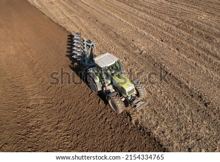 Tractor with plow on soil cultivating. Tractor plowing field, top view. Cultivated land and soil tillage. Agricultural tractor on field cultivation. Tractor disk harrow on plowing ground of field. 