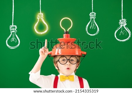 Smart child in the class against blackboard. Funny kid with lightbulb at school. Education, start up and business idea concept Royalty-Free Stock Photo #2154335319