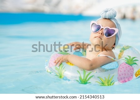 Funny baby girl on summer vacation. Child having fun in swimming pool. Sweet toddler swimming in a floating ring in a pool. Water park. Holidays. Royalty-Free Stock Photo #2154340513