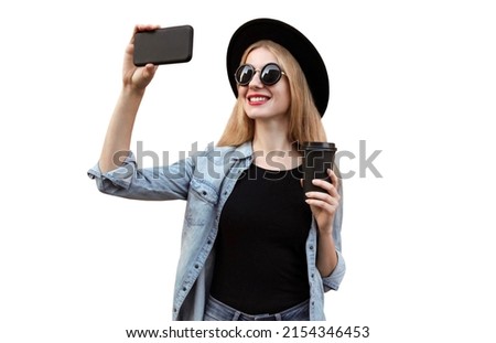 Portrait of happy smiling young woman taking selfie by smartphone wearing black round hat isolated on white background