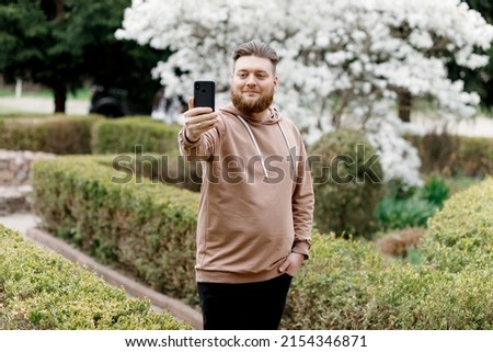 The guy cheerfully takes a selfie on the background of magnolia. Communicates via video call. shows the nature around him.