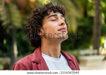 Tranquility. Portrait of a happy caucasian curly man relaxing with closed eyes while standing at the street at the park. Stock photo 