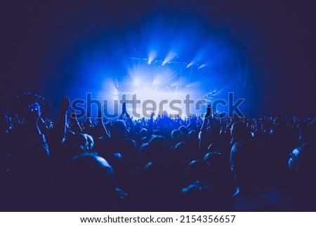 A crowded concert hall with scene stage lights in blue tones, rock show performance, with people silhouette, on a dance floor air during a concert festival Royalty-Free Stock Photo #2154356657