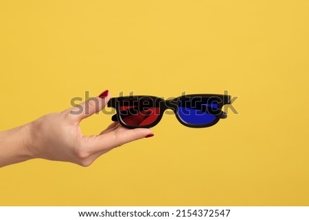Profile side view closeup of woman hand holding and showing 3d eyeglasses for watching movie in cinema. Indoor studio shot isolated on yellow background.