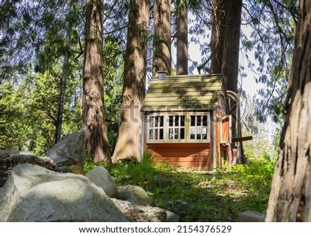 Wooden playhouse made of wood. Brown small house between large trees. Wooden fairytale treehouse, playing house on children playground. Nobody, travel photo, selective focus Royalty-Free Stock Photo #2154376529