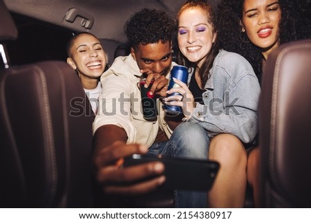 Friends taking a selfie inside a car at night. Group of happy young friends smiling cheerfully while posing for a group photo. Carefree friends taking a ride home after a party.