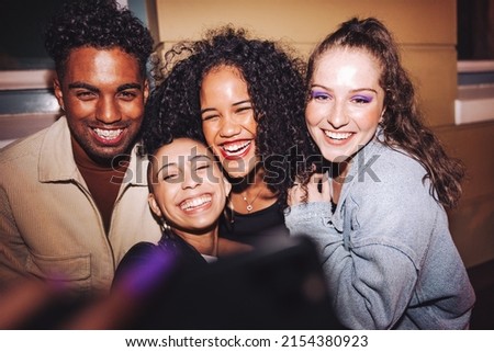 Taking happy selfies on friends night out. Group of multicultural friends taking a group selfie while standing outdoors at night. Cheerful young people having a good time on the weekend.