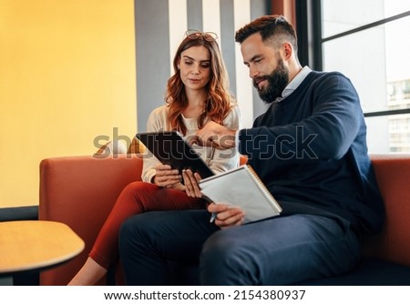 Business associates using a digital tablet in an office lobby. Two modern businesspeople having an important discussion in a co-working space. Two young entrepreneurs collaborating on a new project. Royalty-Free Stock Photo #2154380937