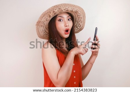 Excited and shocked Asian woman pointing finger at smartphone in her hand, Emotionally reacting to new app isolated over white studio background